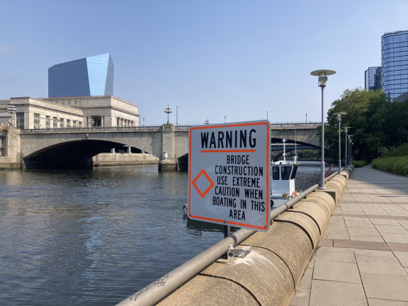 Construction sign posted alongside the river in front of the Market Street Bridge, saying "Warning: bridge construction, use extreme caution when boating in this area"