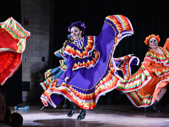Dancers in colorful dresses and Dia de los Muertos face paint