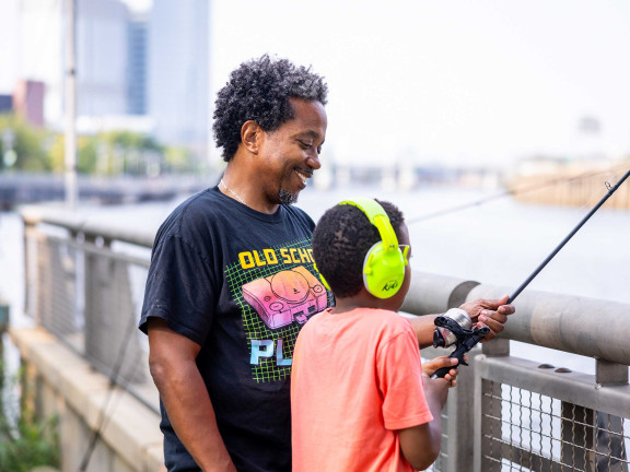 Adult and child fishing along the Schuylkill River on a sunny day