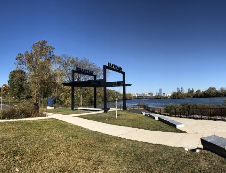 A paved path curves through a grassy park and past a sculpture of steel bars.