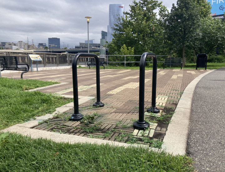 Simple black bike racks near the river, situated in brick with the cityscape behind. 
