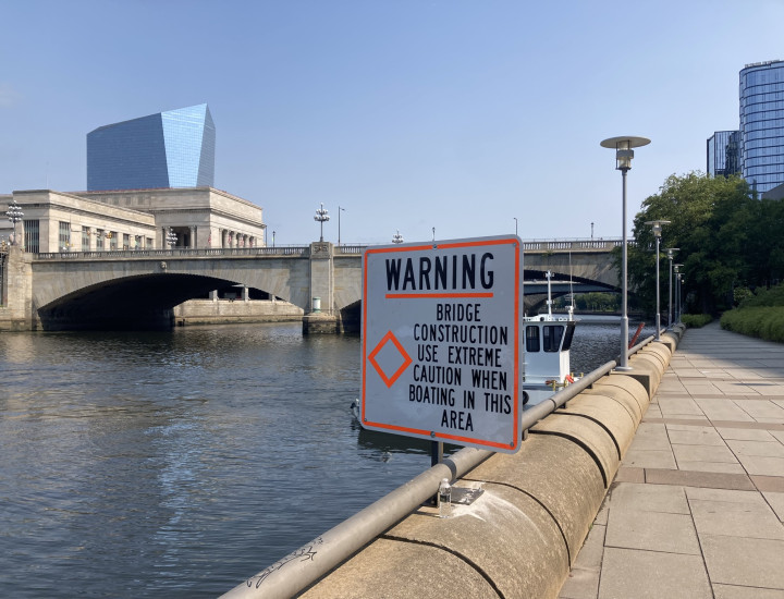 Construction sign posted alongside the river in front of the Market Street Bridge, saying "Warning: bridge construction, use extreme caution when boating in this area"