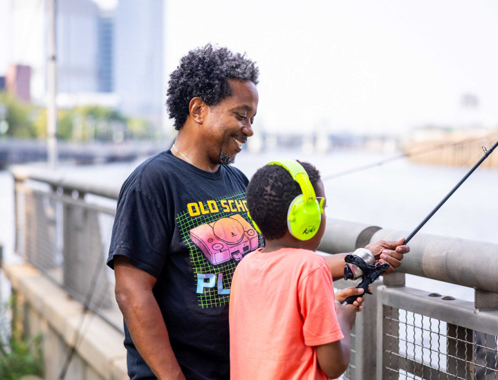 Adult and child fishing along the Schuylkill River on a sunny day